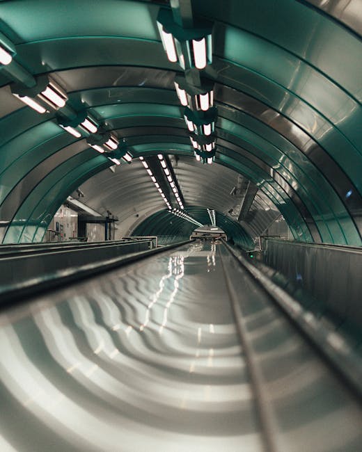 Interior view of a pedestrian underpass beneath the Rotherhithe Tunnel with graffiti-covered brick walls on either side. Fluorescent ceiling lights illuminate the space, leading towards a white direct